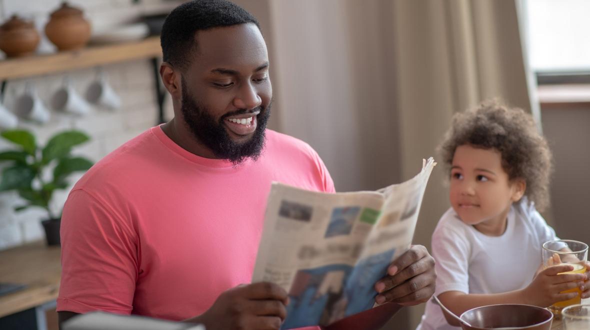 Dad reading the paper at the table next to a child