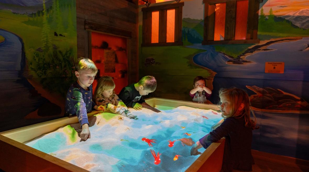 Children playing at the Hands On Children's Museum at an augmented reality sand table