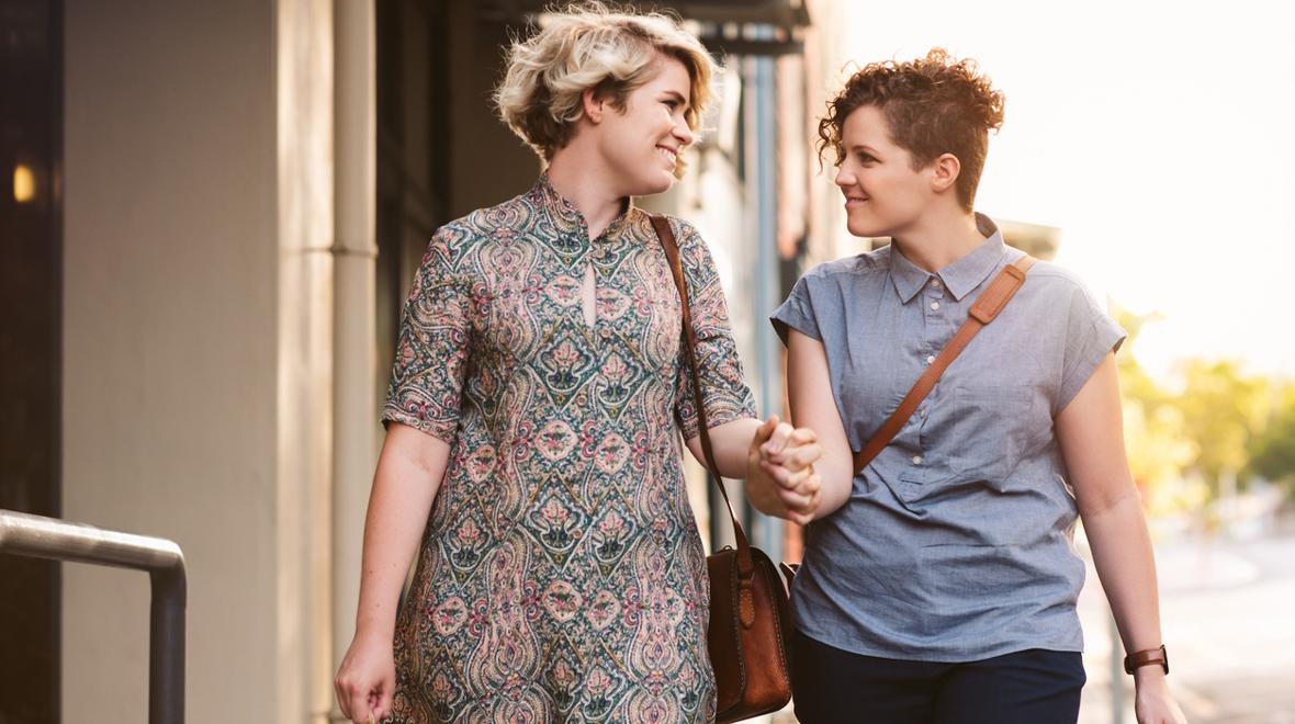 two woman walking down the street holding hands and smiling at each other