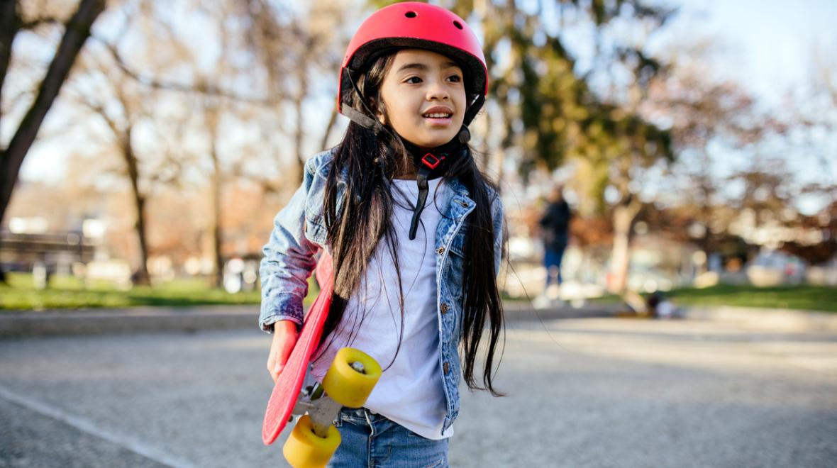 confident child walking with her skateboard while wearing a helmet