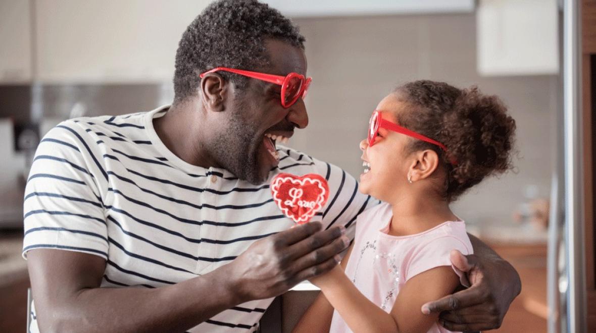 A dad and daughter wearing heart sunglasses, a useful valentine gift for kids while exchanging a red heart