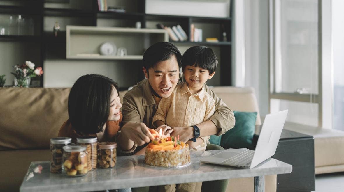 parents with a child celebrating a birthday with a small cake in their living room