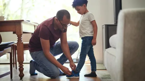 dad tying son shoe kneeling down helping child