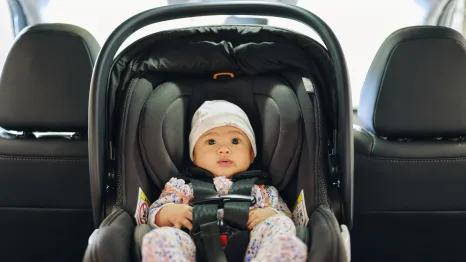 A baby in a rear-facing, safety-stickered car seat in the backseat of a car