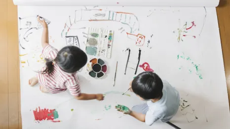 Two siblings painting on butcher paper together