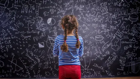 child standing looking at a blackboard covered with math