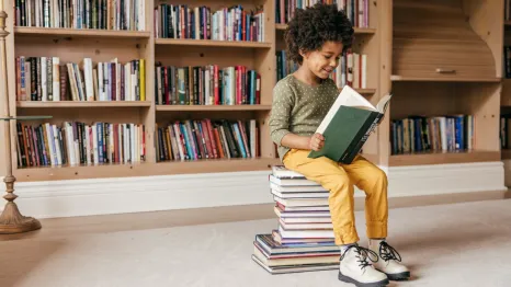 child sitting on a stack of books reading