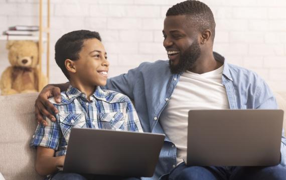 Dad and son on the couch each holding a laptop as they participate in nanowrimo