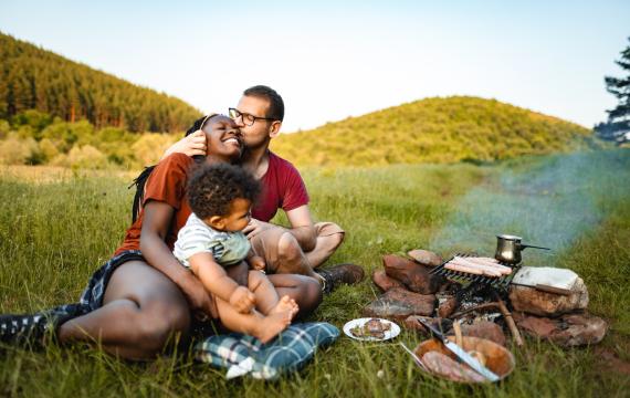 family cooks a meal over a fire while having fun camping