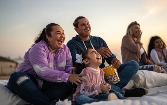 Family on a blanket with popcorn, using outdoor gear for a summer movie