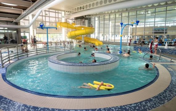 View of people swimming in Rainier Beach indoor Pool in Seattle. Yellow twister slide is in the background and the lazy river feature is in the foreground