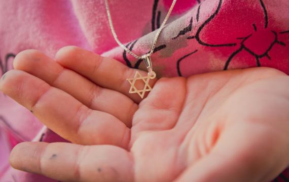 a Jewish child holding a necklace with a Star of David charm