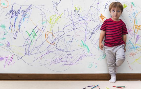 Childing standing in front of a wall that he has colored all over, challenging behavior in kids