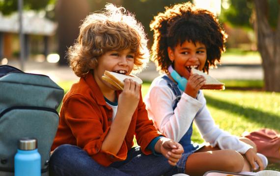 two kids sitting in the grass eating a healthy lunch at summer camp