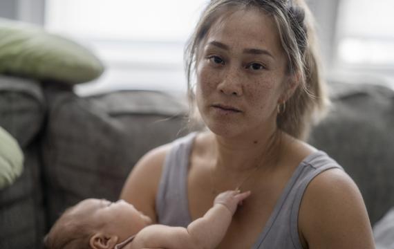 an overwhelmed mom looks into the camera while holding her baby