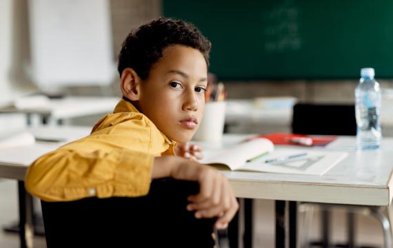 elementary-age student in an empty classroom looking back at the camera