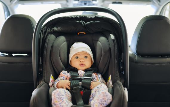 A baby in a rear-facing, safety-stickered car seat in the backseat of a car