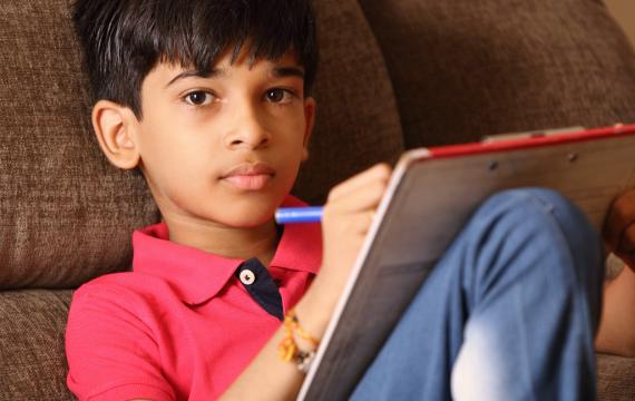 young boy writing in a note pad by himself looks at the camera with a serious expression