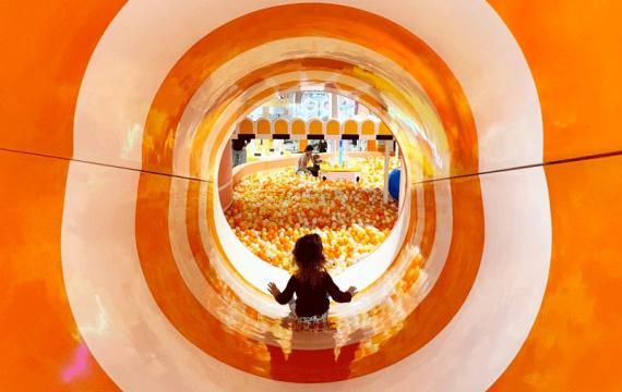 Young girl at an indoor playground slides down the colorful slide into the ball pit at Twinkle Land Play Cafe 