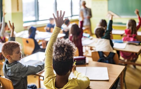 Classroom at school full of students, several raising their hands to answer a question