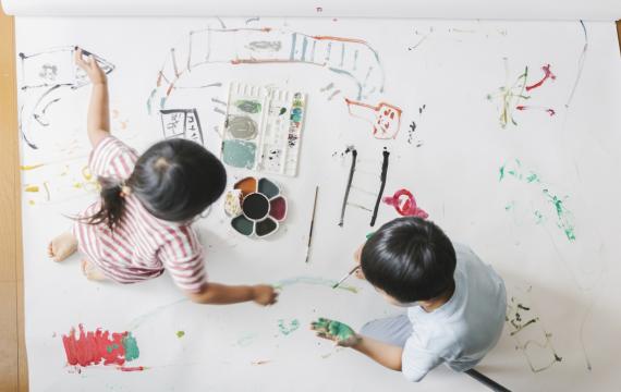 Two siblings painting on butcher paper together