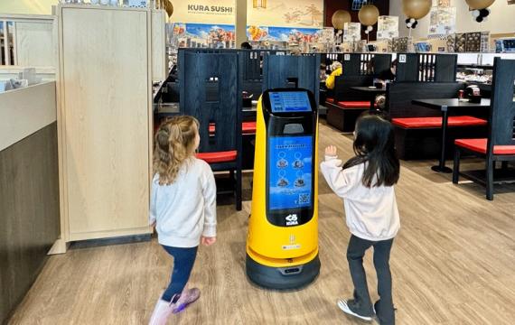 A robot greets two kids at Kura Sushi, a Seattle-area robot restaurant with a sushi conveyor belt