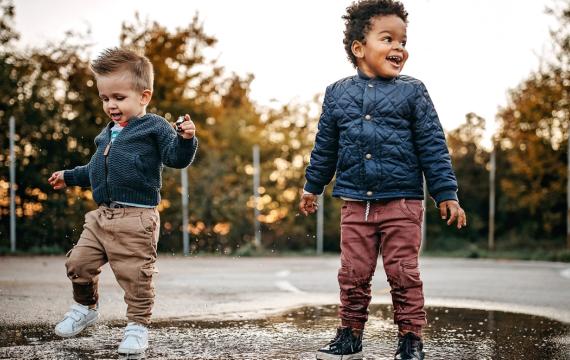 Two little kids playing in a puddle at a park on a rainy day