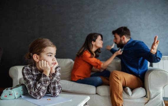 parents arguing in the background while a little girl is stressed in the foreground