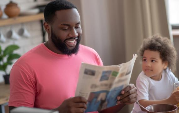 Dad reading the paper at the table next to a child