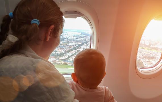 mom and baby on an airplane looking out the window and a city below