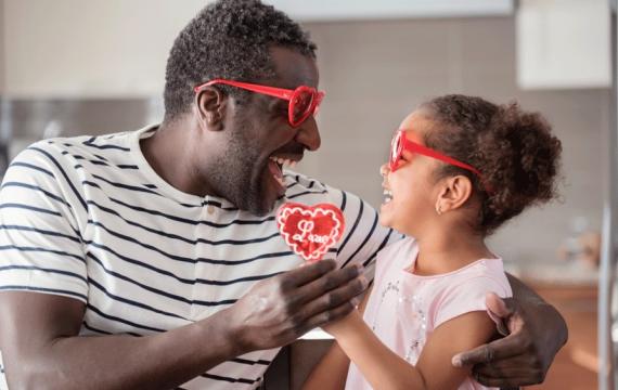 A dad and daughter wearing heart sunglasses, a useful valentine gift for kids while exchanging a red heart