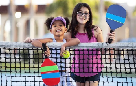 Two girls smiling on a summer day on a pickleball court near Seattle, one of many sports activities to try