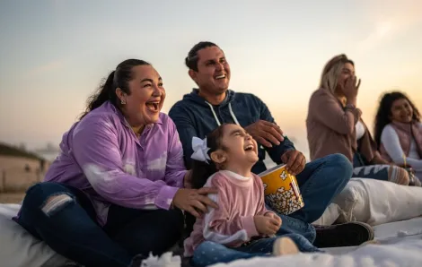 Family on a blanket with popcorn, using outdoor gear for a summer movie