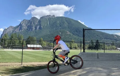 Young boy rides a bike on a Seattle-area pump track with mountain views in the background at Torguson Park in North Bend 