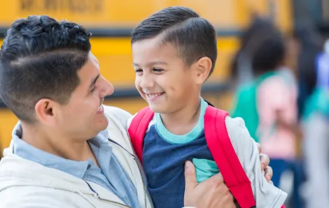 Boy with a red backpack smiling with is father because he's overcome school anxiety