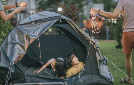 Family setting up a tent and a string of lights for backyard camping