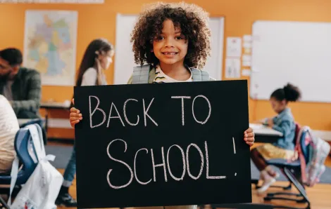 Young girl on first day of school holding up a back-to-school sign