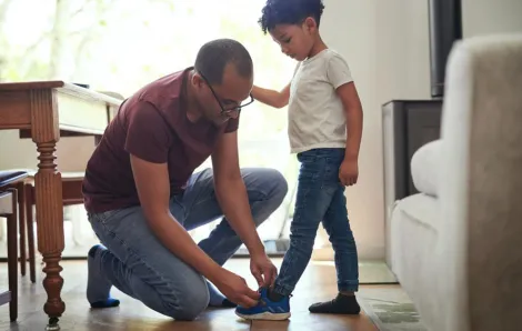 dad tying son shoe kneeling down helping child