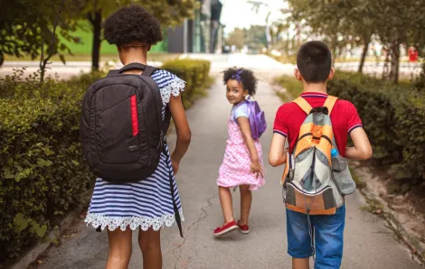 Three kids walking down the sidewalk to school together