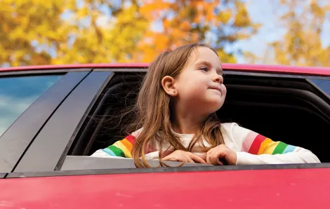 Girl with her head out the window of a car looking at fall leaves on a scenic drive in the Pacific Northwest