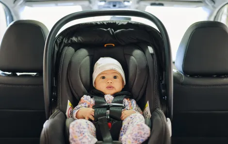 A baby in a rear-facing, safety-stickered car seat in the backseat of a car