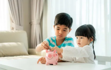 Kids learning to save money putting coins in a piggy bank