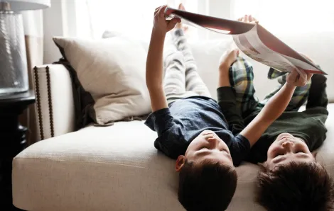 Brothers reading a book together on a couch upside-down 