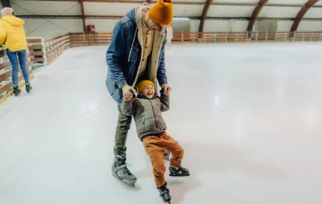 Boy and his dad learning to ice skate at an outdoor holiday ice-skating rink near Seattle