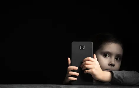 a young child from the anxious generation with a cell phone in hand against a dark background