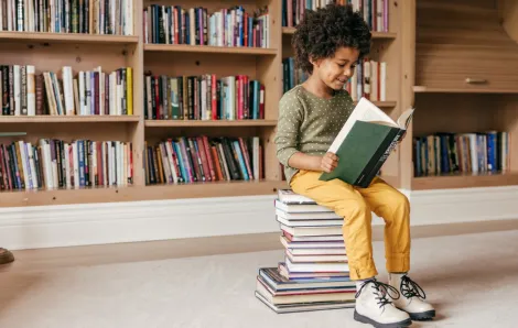 child sitting on a stack of books reading