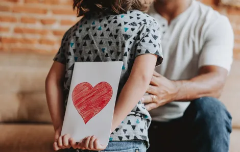 child holding a valentine behind their back for their parent