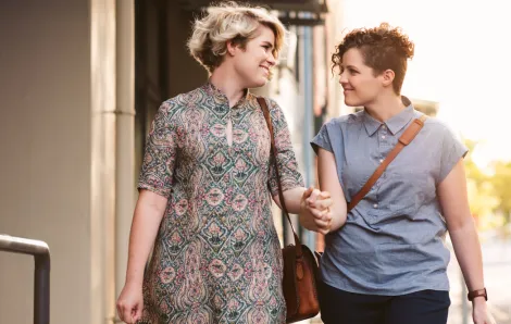 two woman walking down the street holding hands and smiling at each other