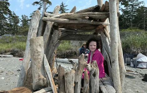 young girl in a driftwood fort on Deception Pass State Park beach, with a nearby campground for families