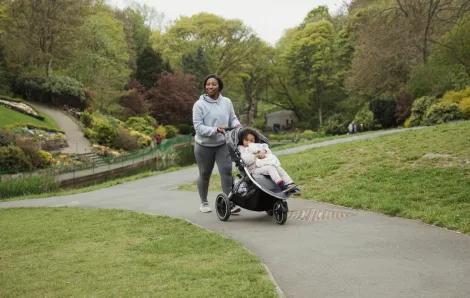 mom pushing a stroller down a park path